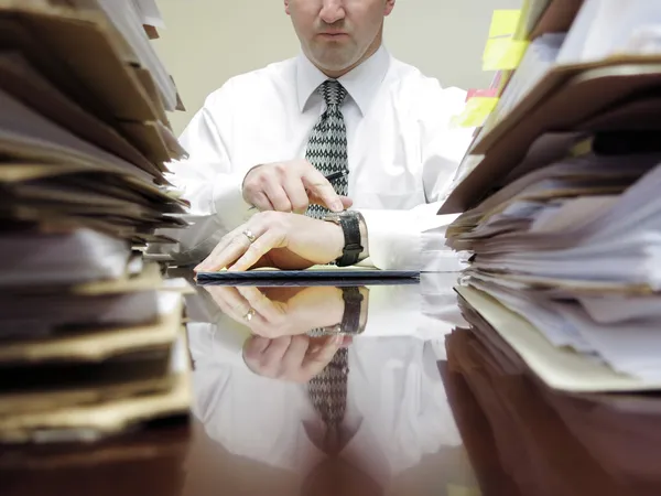 Empresario en el escritorio con archivos apuntando al reloj — Foto de Stock