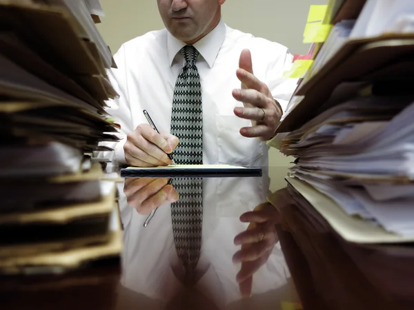 Uomo d'affari alla scrivania con file gesticolando — Foto Stock