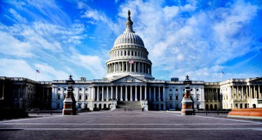 Amerika Birleşik Devletleri Kongre Binası. Rüzgarda ve sütunlarda dalgalanan Amerikan bayrağı. Mavi gökyüzü ve arka planda bulutlar.