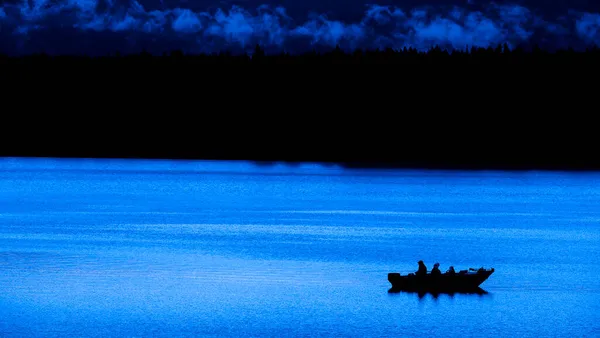 黄昏或黎明时分在湖上的船上钓鱼的人 — 图库照片