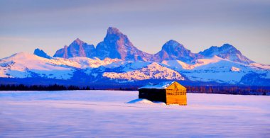 Teton Dağları, kışın Sunset Light Grand Tetons ve tarlada eski bir kulübe.