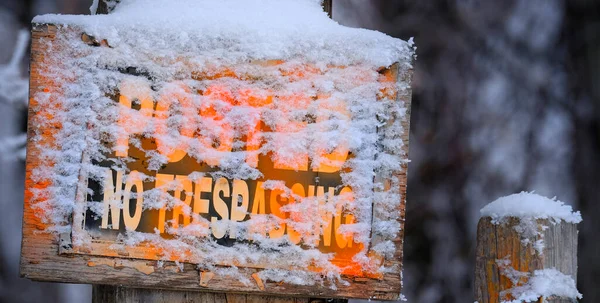 No trespassing sign posted on a wooden fence post in winter with snow orange notice warning