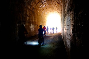Group of people bikers biking through dark tunnel with headlights on Hiawatha Trail