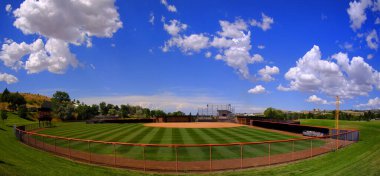 Manicured mowed grass lines on a baseball field diamond with blue sky and clouds summer day