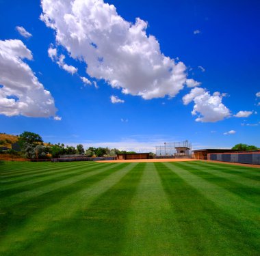 Manicured mowed grass lines on a baseball field diamond with blue sky and clouds summer day