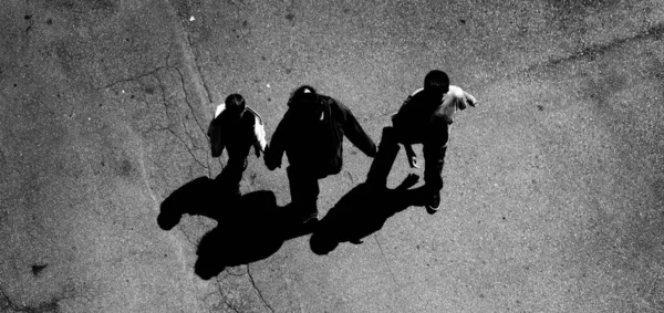 Several people walking down below on concrete with shadows aerial view from above