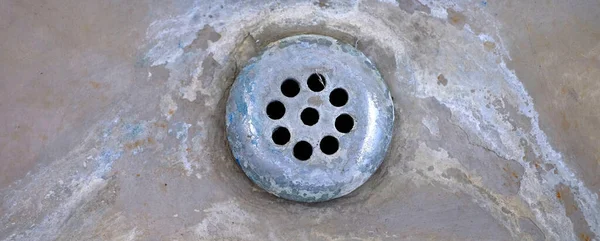 Old worn drain in sink or tub with mineral deposits and stains around holes