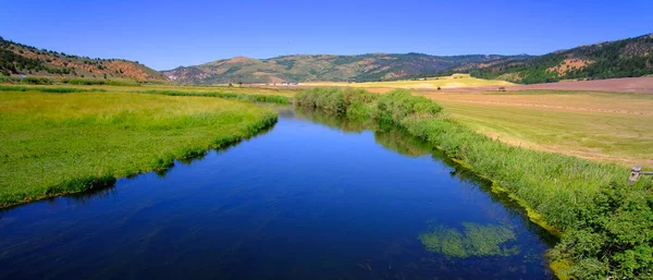 Blue strea or river of flowing water in valley reflecting blue sky and clouds