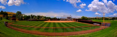 Manicured mowed grass lines on a baseball field diamond with blue sky and clouds summer day