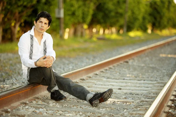 ラテン系男性の鉄道線路の上に座って — ストック写真