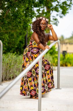 Tropikal bir ortamda renkli bir elbise içinde poz veren çok ırklı güzel bir kadın model.