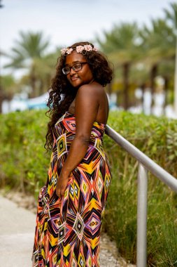 Tropikal bir ortamda renkli bir elbise içinde poz veren çok ırklı güzel bir kadın model.