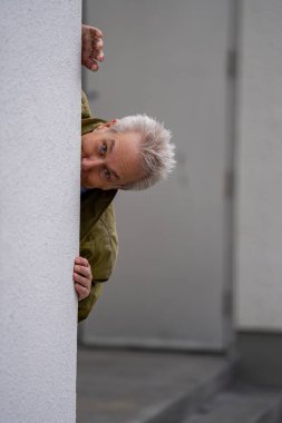 İş adamı binanın arkasından kafasını yana doğru dikizliyor.