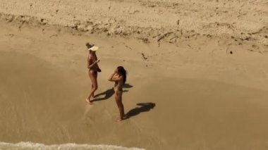 Sahilde yürürken arkadaşının videosunu çeken bir kadın. 4k yakın çekim hava görüntüsü