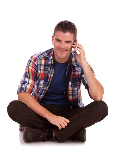 Jovem sentado sorrindo ao telefone — Fotografia de Stock