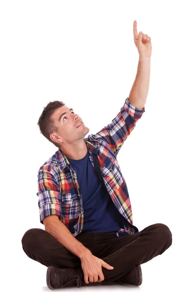 Junger sitzender Mann zeigt nach oben — Stockfoto