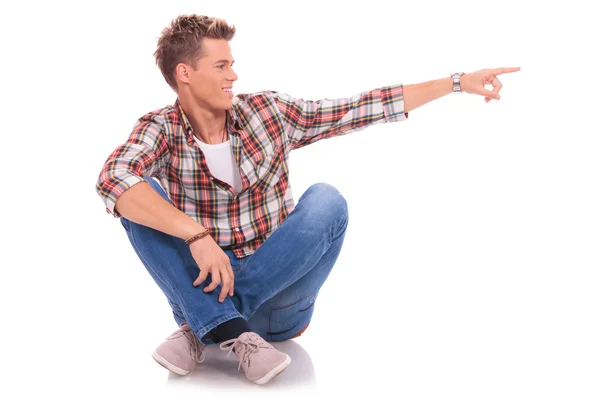 Sentado joven apuntando a un lado —  Fotos de Stock