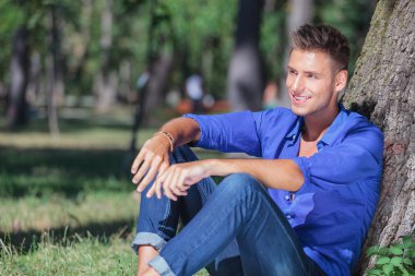 uzakta oturan adamın ağaca yaslanmış görünüyor