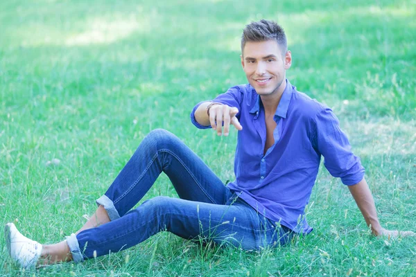 Mann sitzt im Gras und zeigt auf dich — Stockfoto