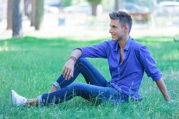 Homem sentado na grama olha para longe — Fotografia de Stock