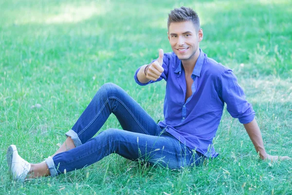 Hombre se sienta en el parque & muestra ok —  Fotos de Stock