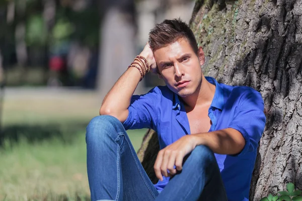 Homem sério senta-se em uma árvore no parque — Fotografia de Stock