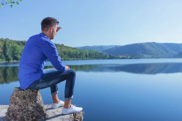 Hombre se sienta junto al lago y mira hacia otro lado — Foto de Stock