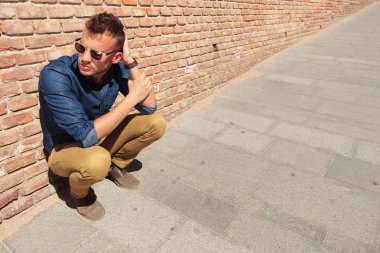 Casual adam tuğla duvar tarafından crouches