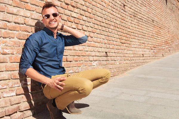 Casual man crouching by wall & smiling — Stock Photo, Image