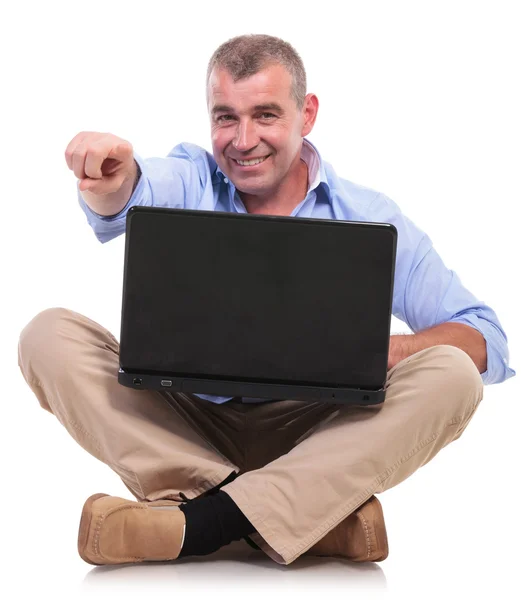 Casual old man sits with laptop and points Royalty Free Stock Images