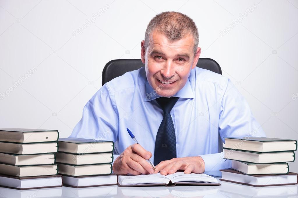 old business man writes at desk full of books