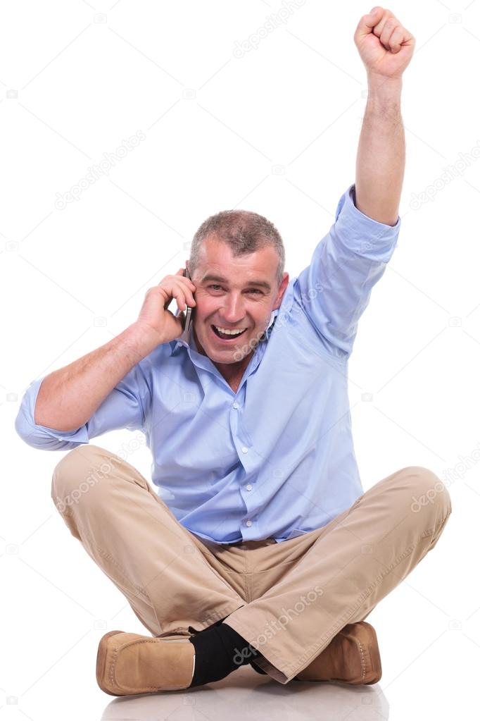 casual old man sits and cheers while on phone