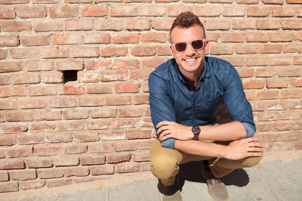 Casual man crouches in front of brick wall — Stock Photo, Image