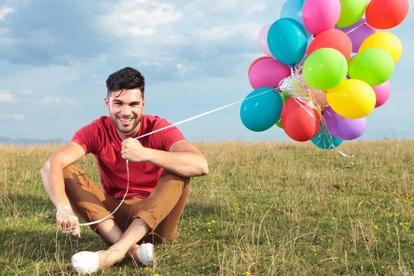 Příležitostné muž sedící v trávě s balónky — Stock fotografie