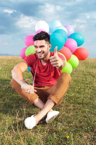 Seduto uomo casual con palloncini mostra pollice in su — Foto Stock