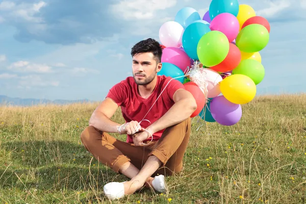 Zittende casual man met ballonnen ziet er weg — Stockfoto