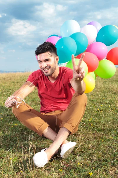 Seated casual man with balloons shows victory — Stock Photo, Image