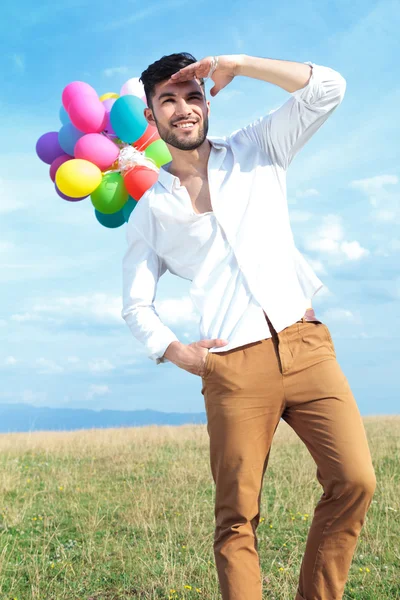 Casual man met ballonnen kijkt ver weg — Stockfoto