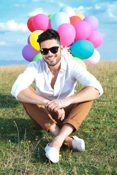 Сидящий мужчина в воздушных шарах и солнцезащитных очках — стоковое фото