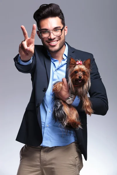 Casual jonge man houdt puppy en toont overwinning — Stockfoto