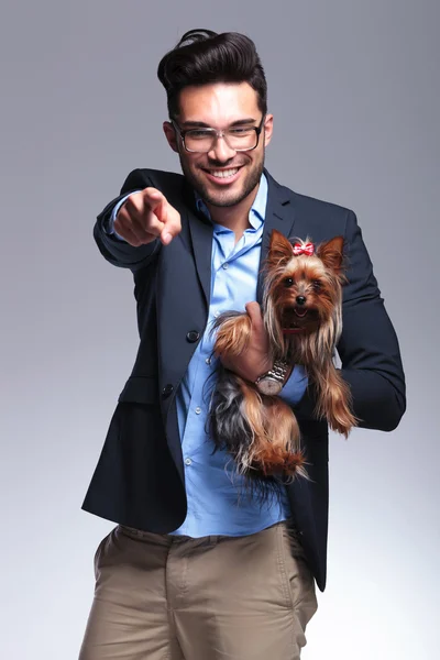 Casual young man holds puppy and points at you — Stock Photo, Image