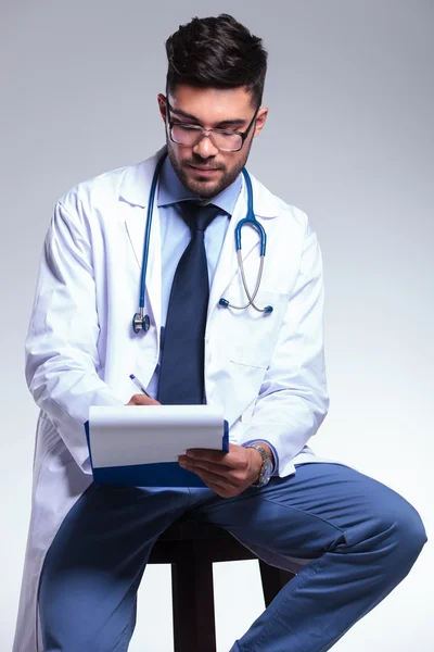 Młody lekarz siedzi i pisze — Zdjęcie stockowe