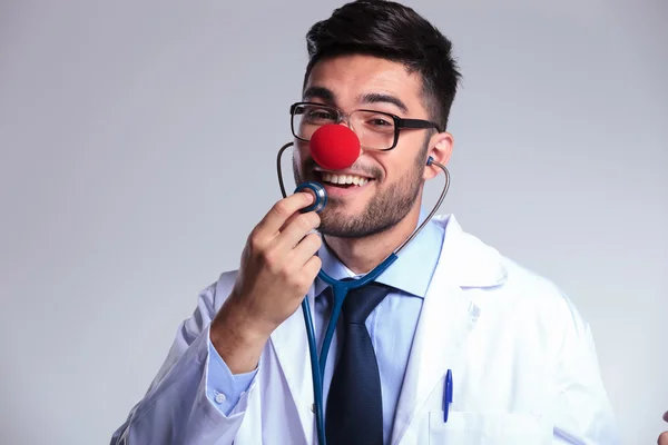 Unga läkare med clown röd näsa lyssnar på själv — Stockfoto