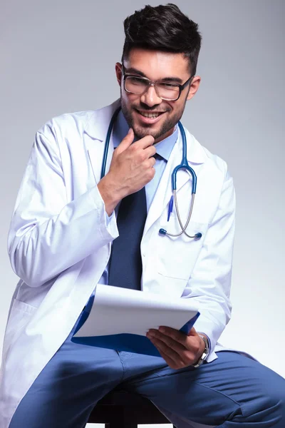 Seated young doctor with hand at chin — Stock Photo, Image