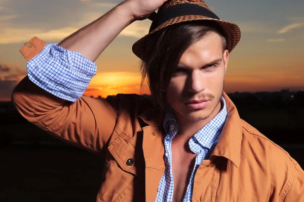 Casual man with hand on hat and the sunset behind — Stock Photo, Image