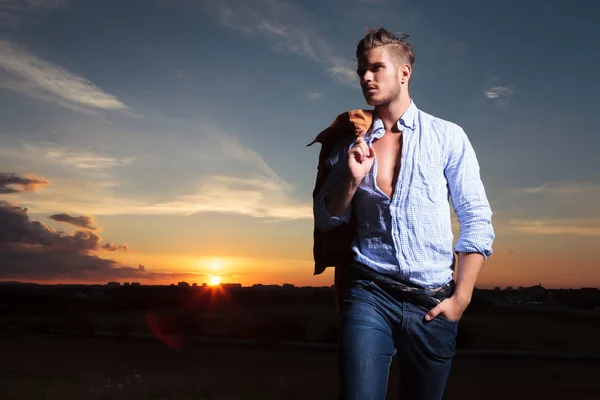 Homem casual com a mão no bolso ao pôr do sol olha para longe — Fotografia de Stock