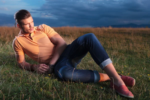 草の中を敷設しながらの距離に見えるカジュアルな男 — ストック写真