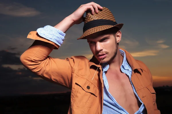 Casual man looks away with straw in mouth and hand on hat — Stock Photo, Image