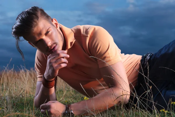 Casual man laying in grass with hand at chin — Stock Photo, Image