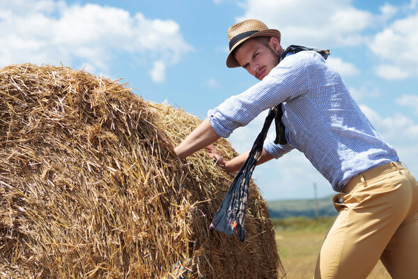 casual man outdoor pushing a big round haystack